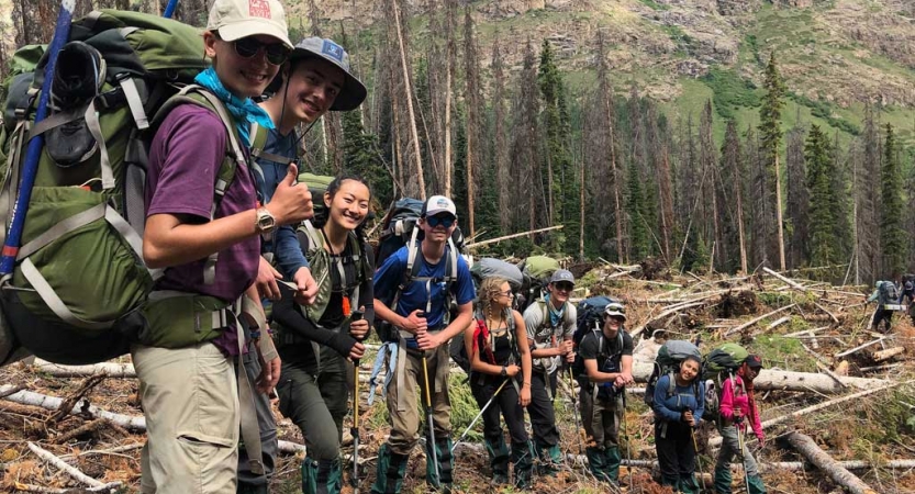 a group of backpacking students smile at the camera amongst felled trees